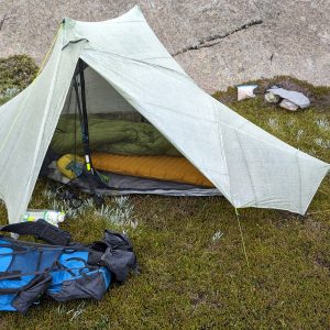 An orange inflatable sleeping pad and sleeping bag laid out inside an ultralight backpacking tent, pack alongside