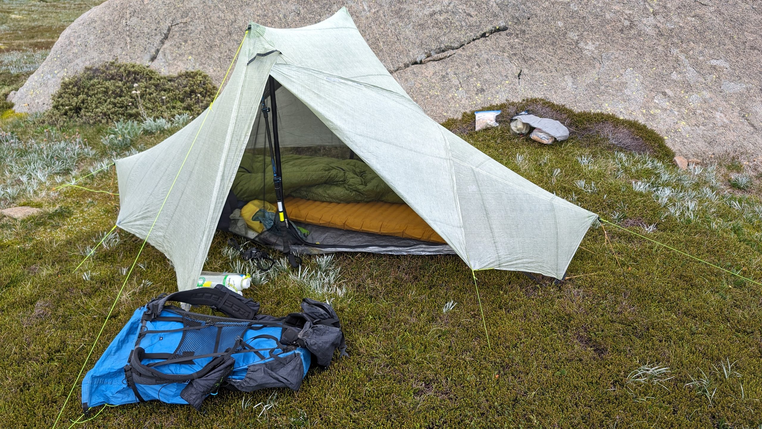An orange inflatable sleeping pad and sleeping bag laid out inside an ultralight backpacking tent, pack alongside