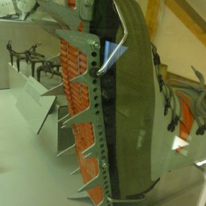 Macro detail of a forged steel mountaineering crampon with orange anti-balling plate mounted on a boot, museum display