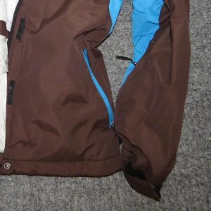 Close-up of a technical hardshell jacket's zippered chest pocket and cuff, showing weatherproof fabric texture and seam construction
