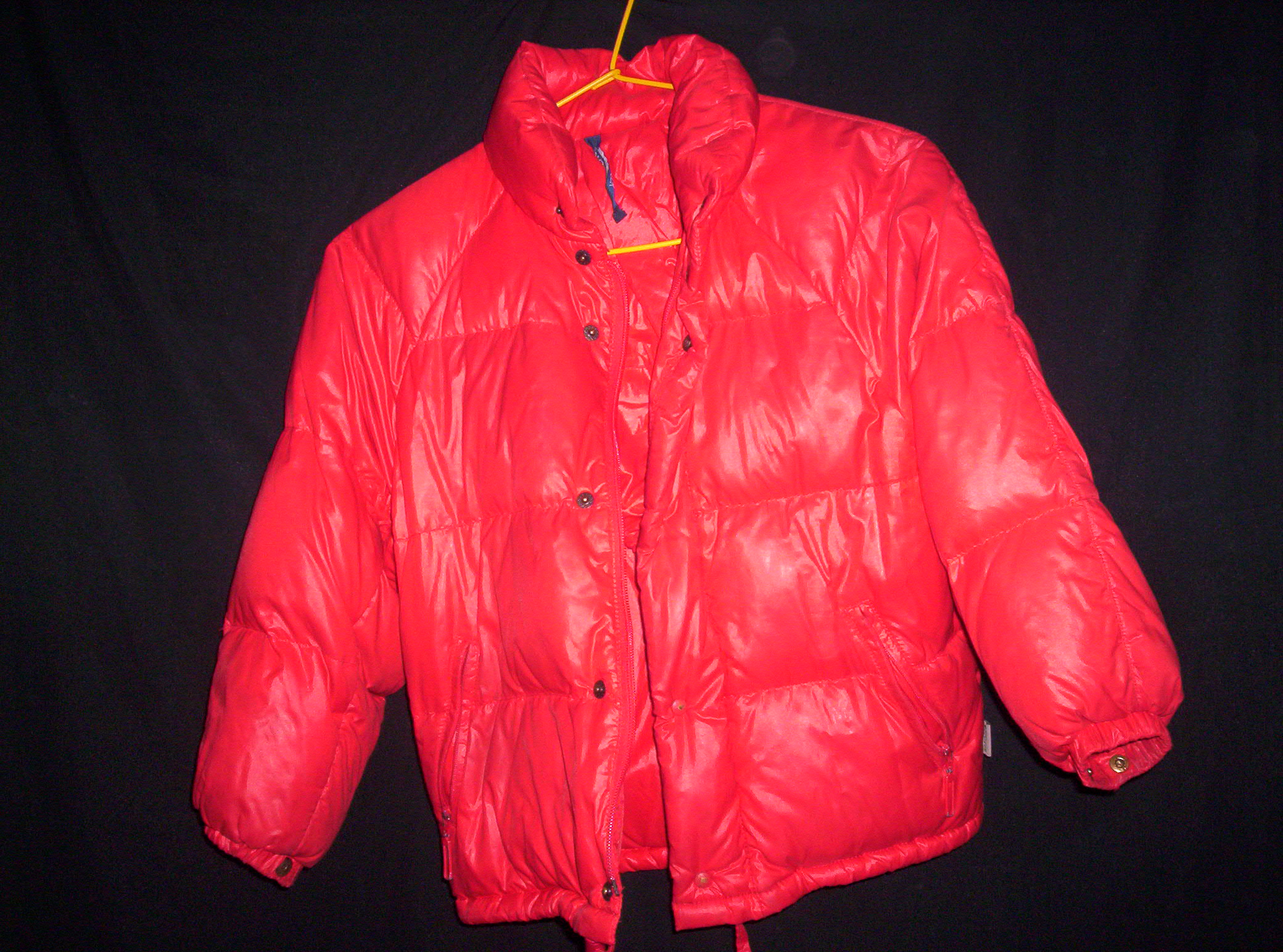 A heavy red insulated down parka hanging on a hanger, showing full puffy baffle construction