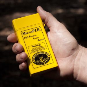 A hand holds a small yellow handheld satellite emergency locator beacon device outdoors