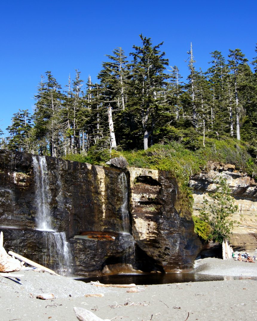 Tsusiat Falls cascading onto the sandy beach below temperate rainforest cliffs on the West Coast Trail, Vancouver Island, Canada